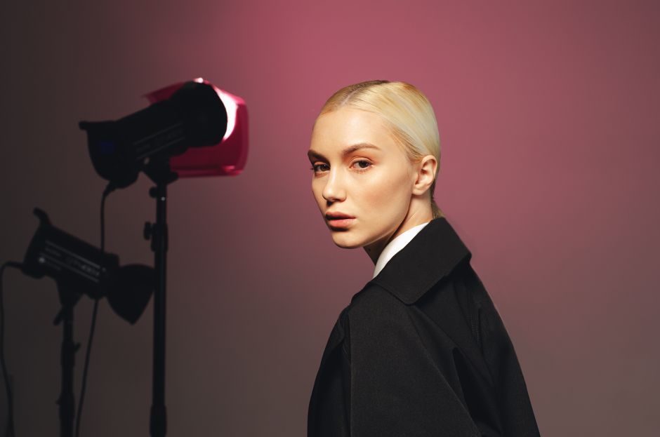 Studio portrait of a blonde woman with elegant attire, featuring dramatic lighting setup.