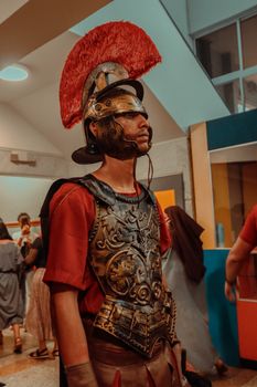 Man dressed as a Roman soldier in ornate armor with a plumed helmet indoors.