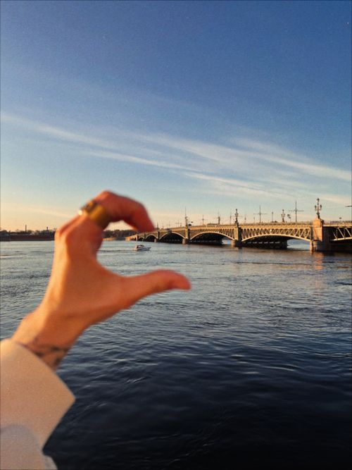 Free A hand framing a picturesque bridge over a calm river under a blue sky. Stock Photo