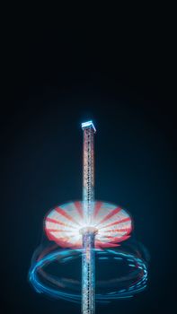 Long exposure of an illuminated carnival ride tower at night, capturing vibrant motion.