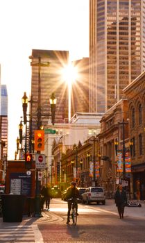 Vibrant city street scene at sunrise with people commuting and modern high-rise buildings.