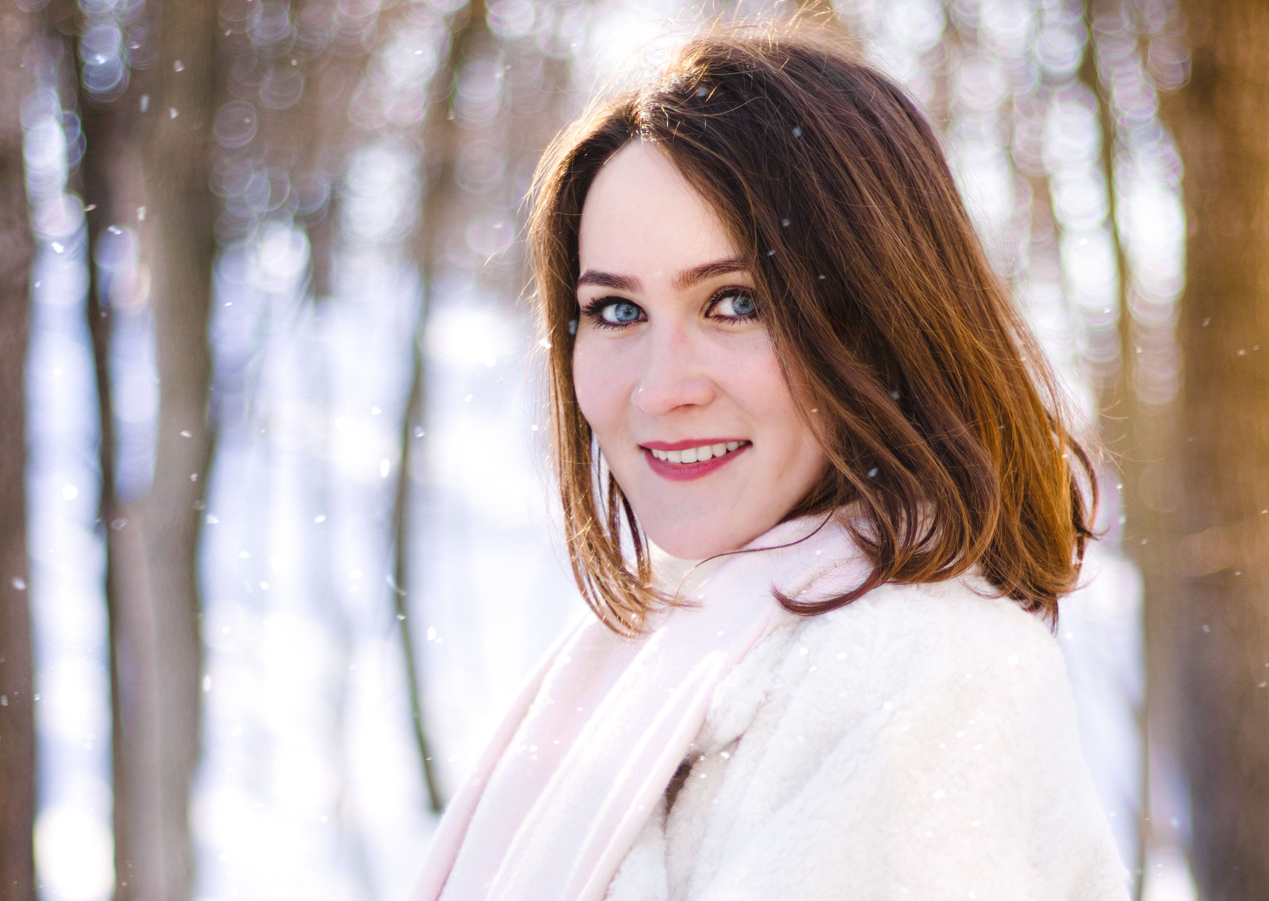 Charming portrait of a woman in winter clothing, smiling in a snowy forest setting.