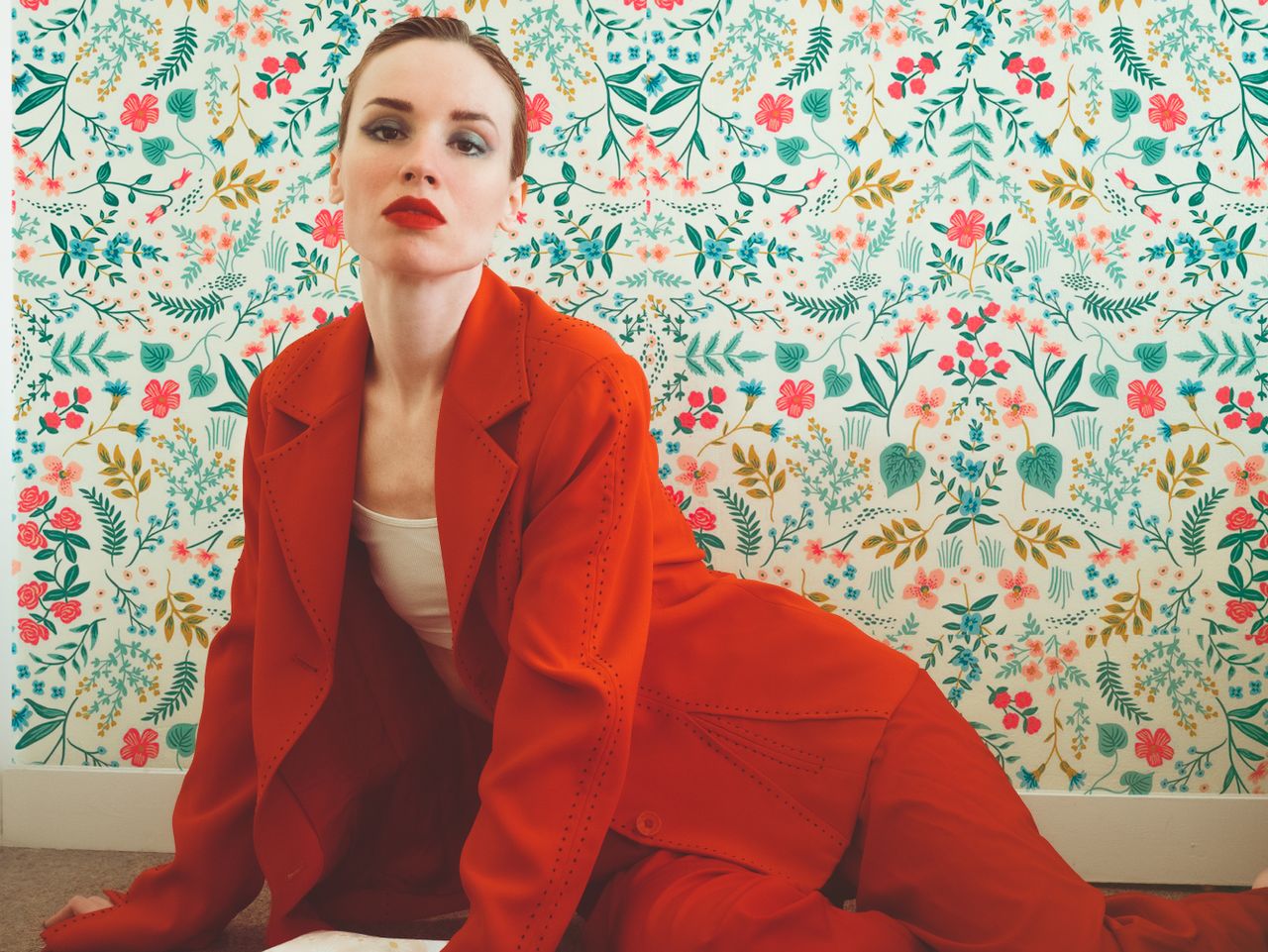 elegant woman in a red suit posing against a vibrant floral background