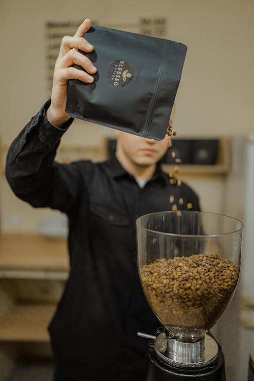 A Man in Black Long Sleeves Pouring Coffee Beans on a Coffee Maker