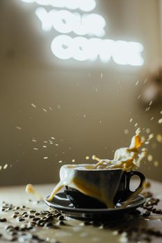Dramatic capture of coffee splashing out of a black cup with beans scattered around.