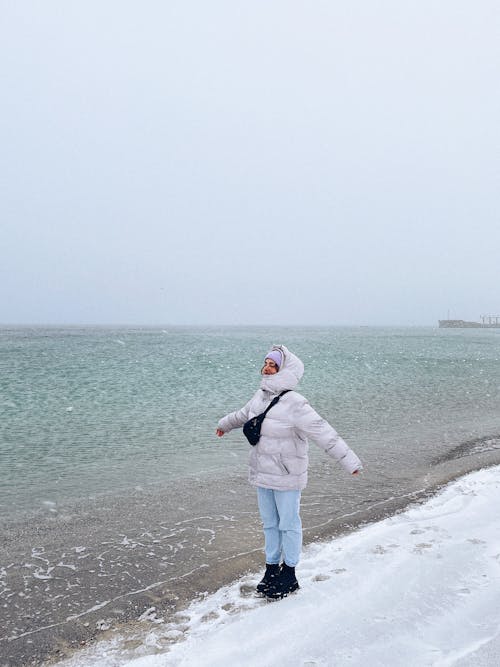 Free Woman Wearing a Puffer Jacket Standing on Shore Stock Photo