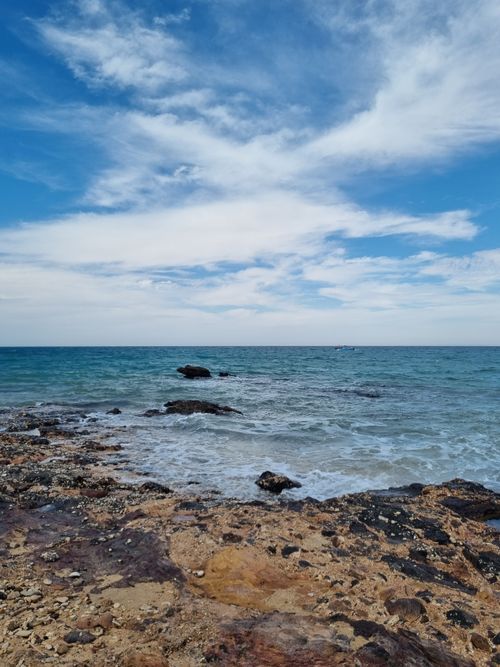 Free Rocky shoreline with vibrant blue sea, scenic view under a bright sky. Stock Photo