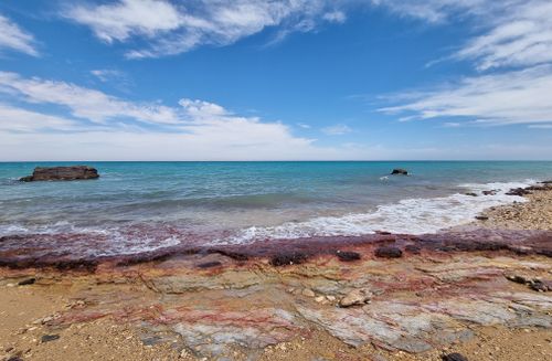 Free Peaceful beach with colorful rocks and clear blue ocean under a bright sky. Stock Photo