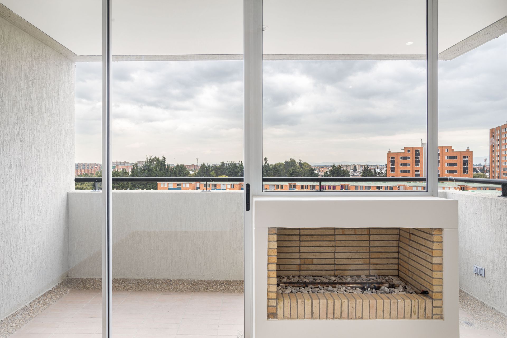 Spacious balcony with glass windows and a brick fireplace overlooking Bogotá cityscape.