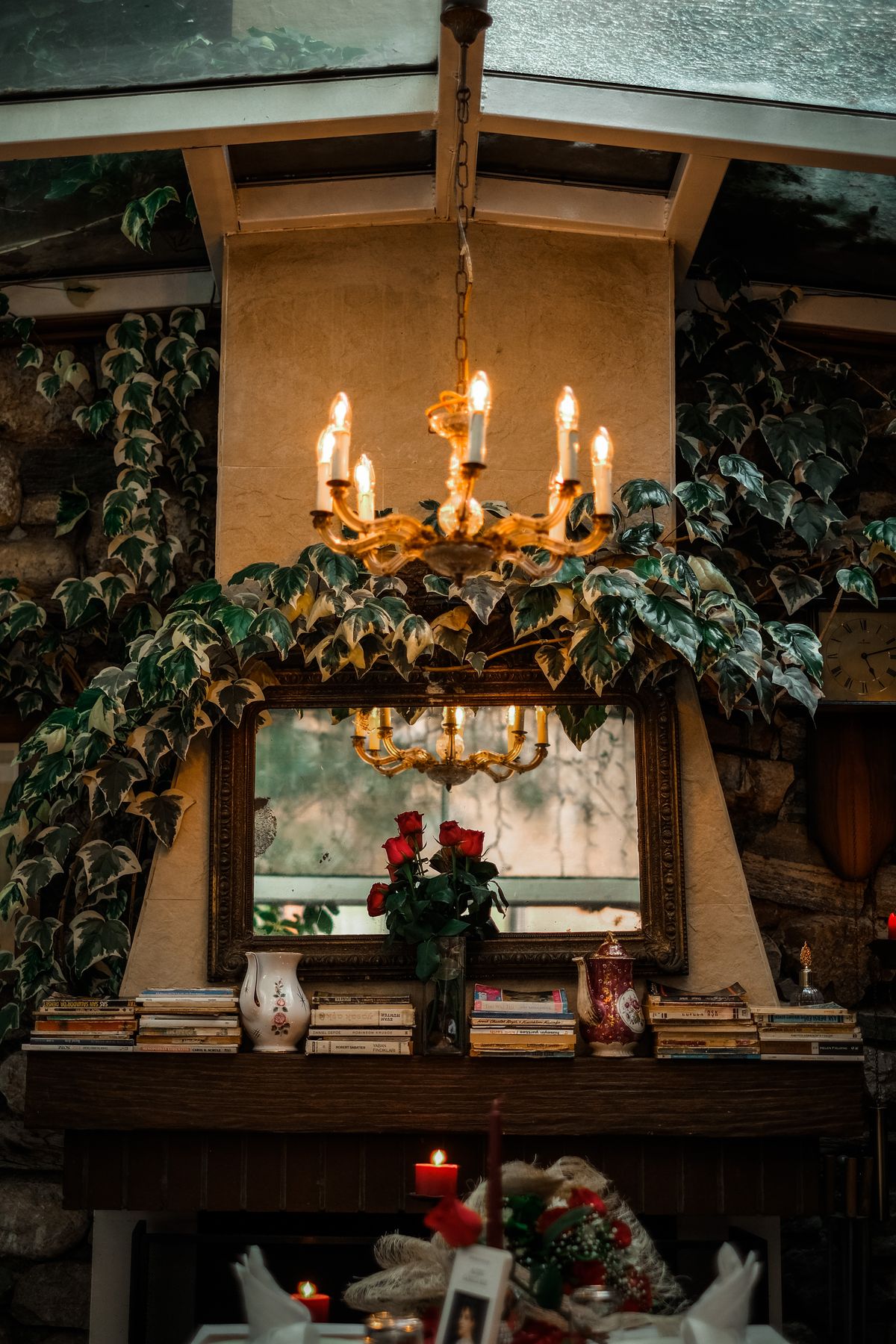 Warm and inviting vintage interior with a decorated fireplace featuring books, flowers, and a chandelier. Stock Photo.