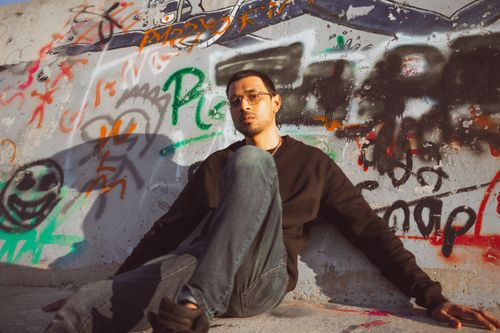 Free Man in casual attire sitting against a colorful graffiti wall, capturing urban art essence. Stock Photo