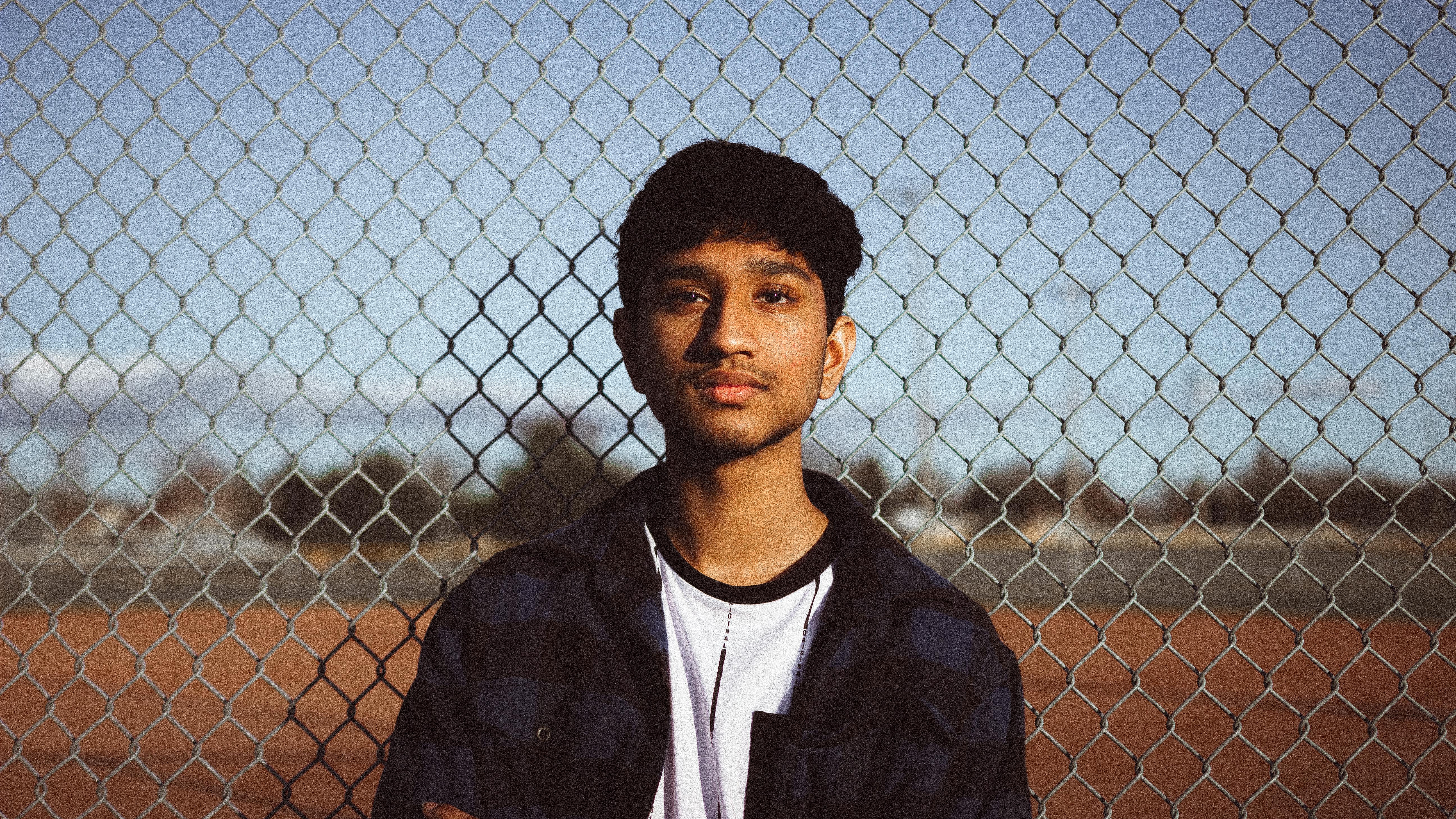 Portrait of a teenage boy standing outdoors against a chain-link fence in natural light.