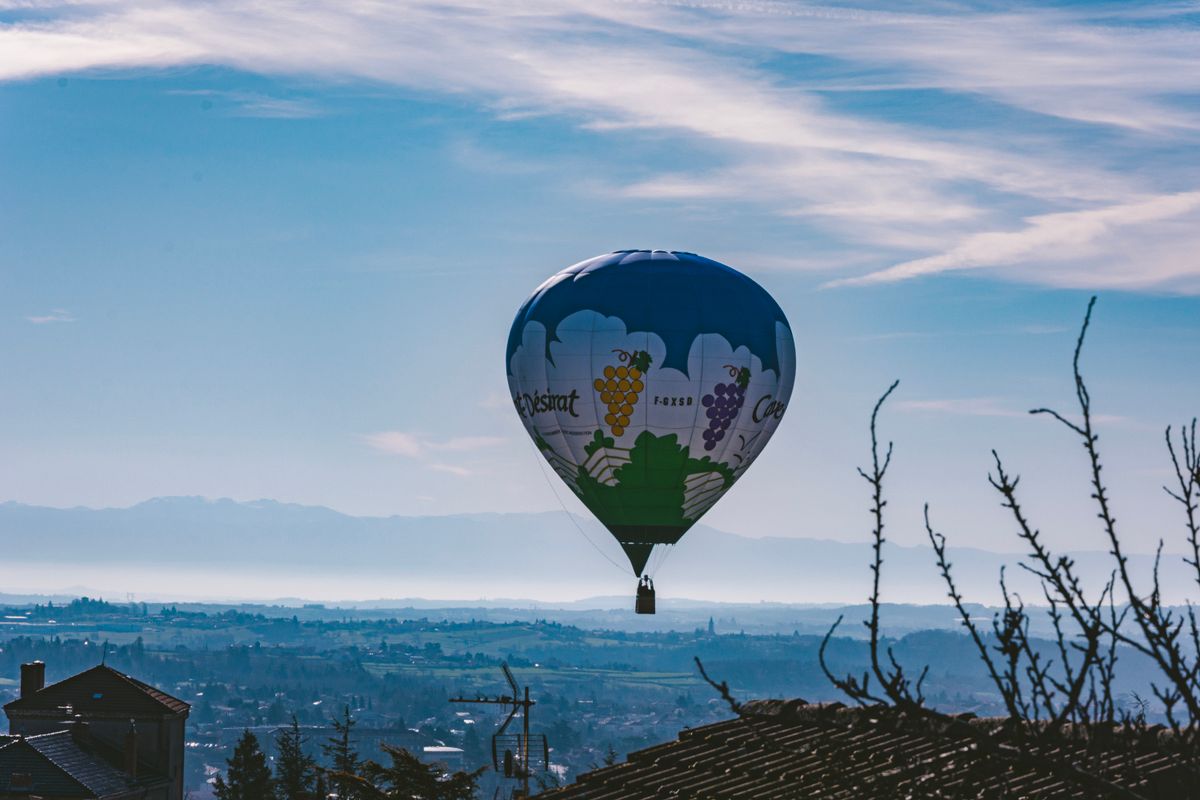 A hot-air balloon drifting over a French valley of vines and rooftops
