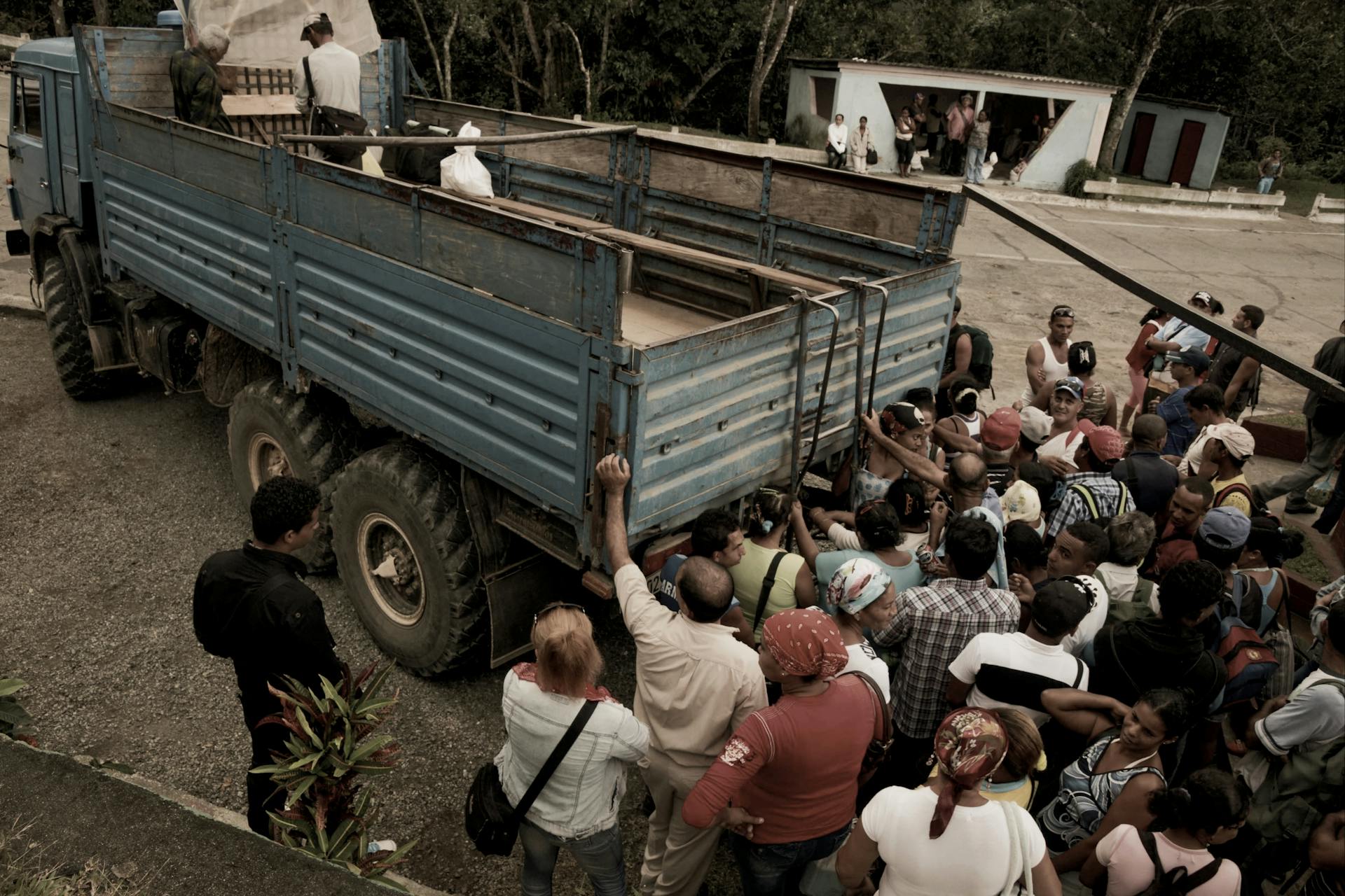A big crowd assembles around a blue cargo truck outdoors, engaging in lively activity.
