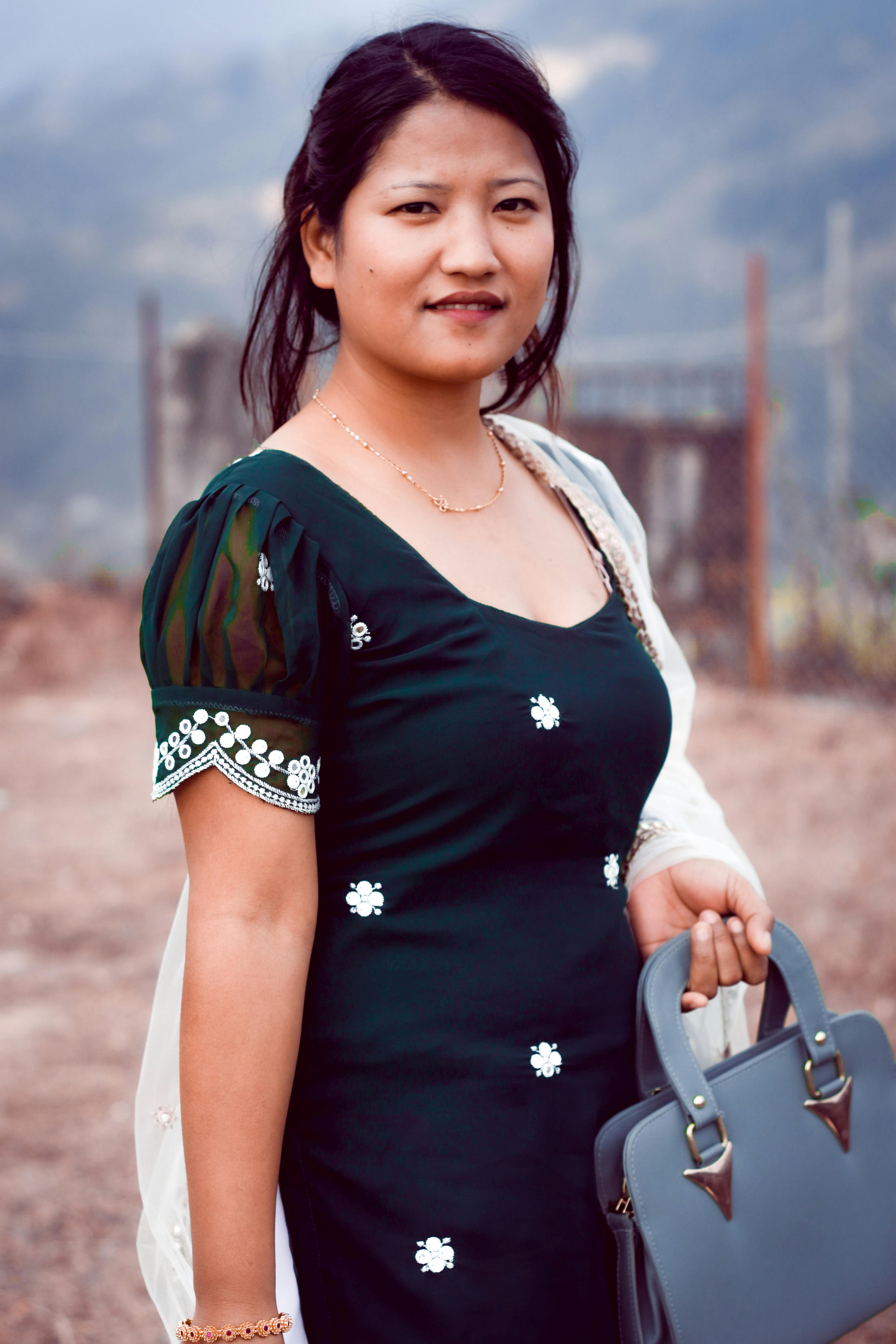 Confident woman in a blue dress holding a handbag outdoors with a smile.