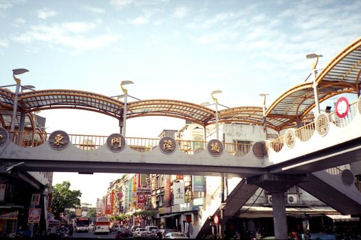A vibrant street scene in Tainan City, Taiwan with a modern elevated footbridge.