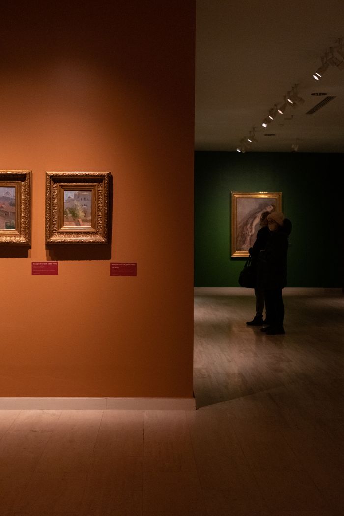 Visitors admiring framed paintings in a warmly lit gallery