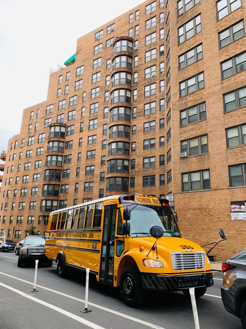 Free A bright yellow school bus parked on an urban street with tall buildings. Stock Photo