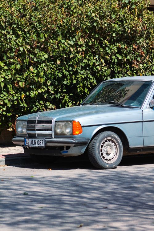 Free A vintage blue sedan parked on a street against a lush green background. Stock Photo