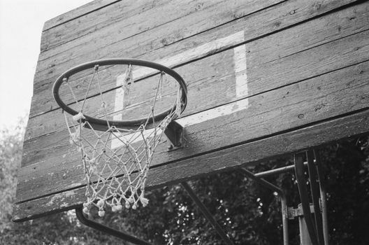 A close-up image of an old, wooden basketball hoop with a net in a grayscale tone.