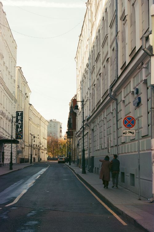 Free A couple walks along an urban street lined with tall buildings, creating a serene cityscape. Stock Photo