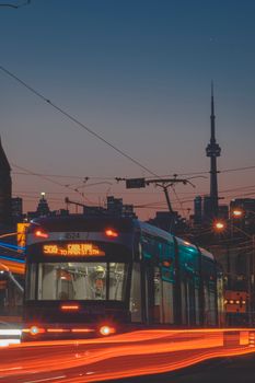 Toronto streetcar passing by CN Tower during twilight, creating a vibrant city scene.
