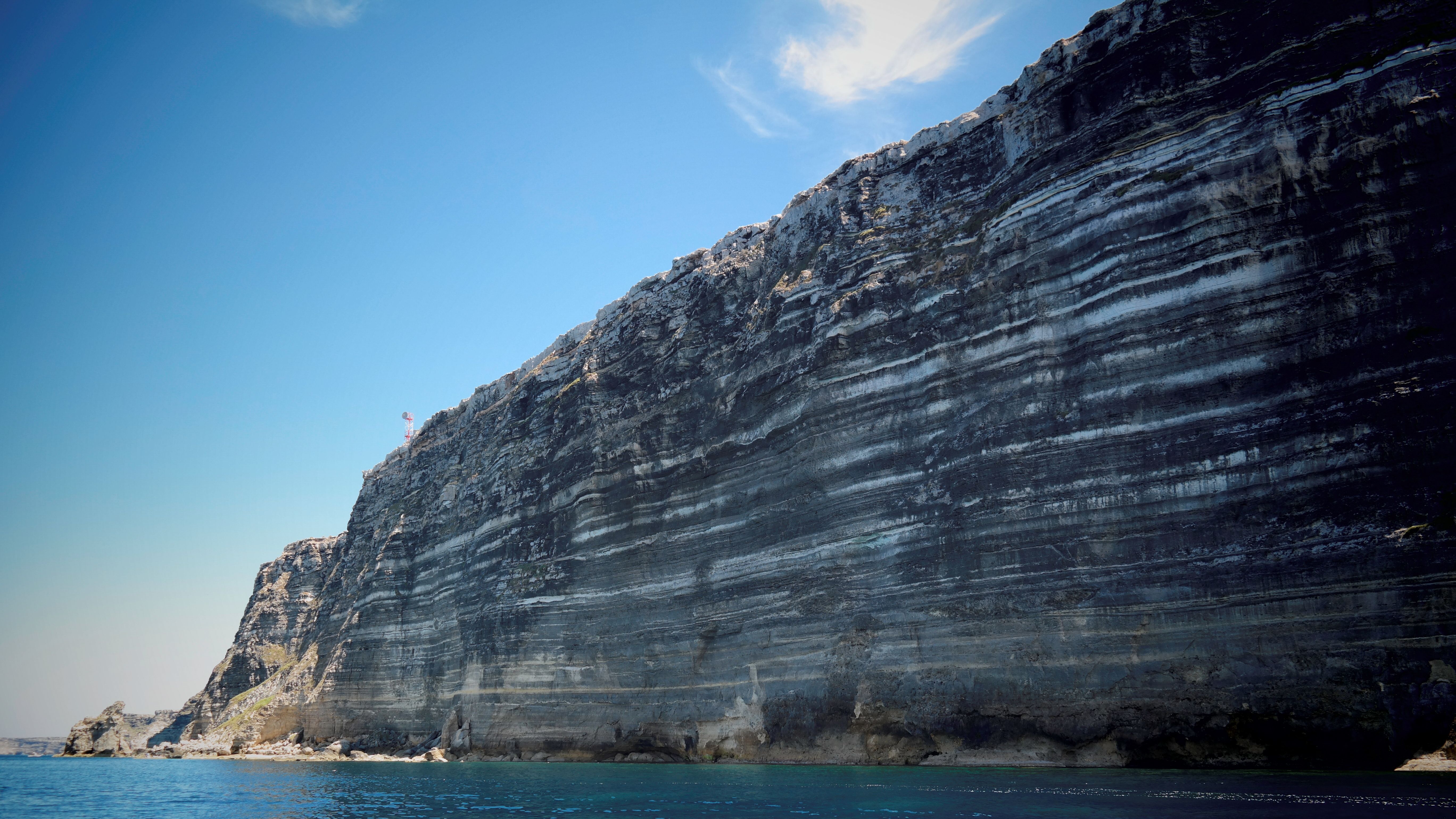 A breathtaking view of a rocky cliff rising from the ocean under a clear blue sky, showcasing natural geological beauty.
