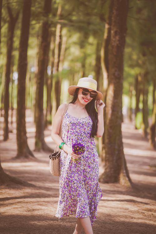 Free Stylish woman in a floral dress and straw hat posing in a sunny forest Stock Photo