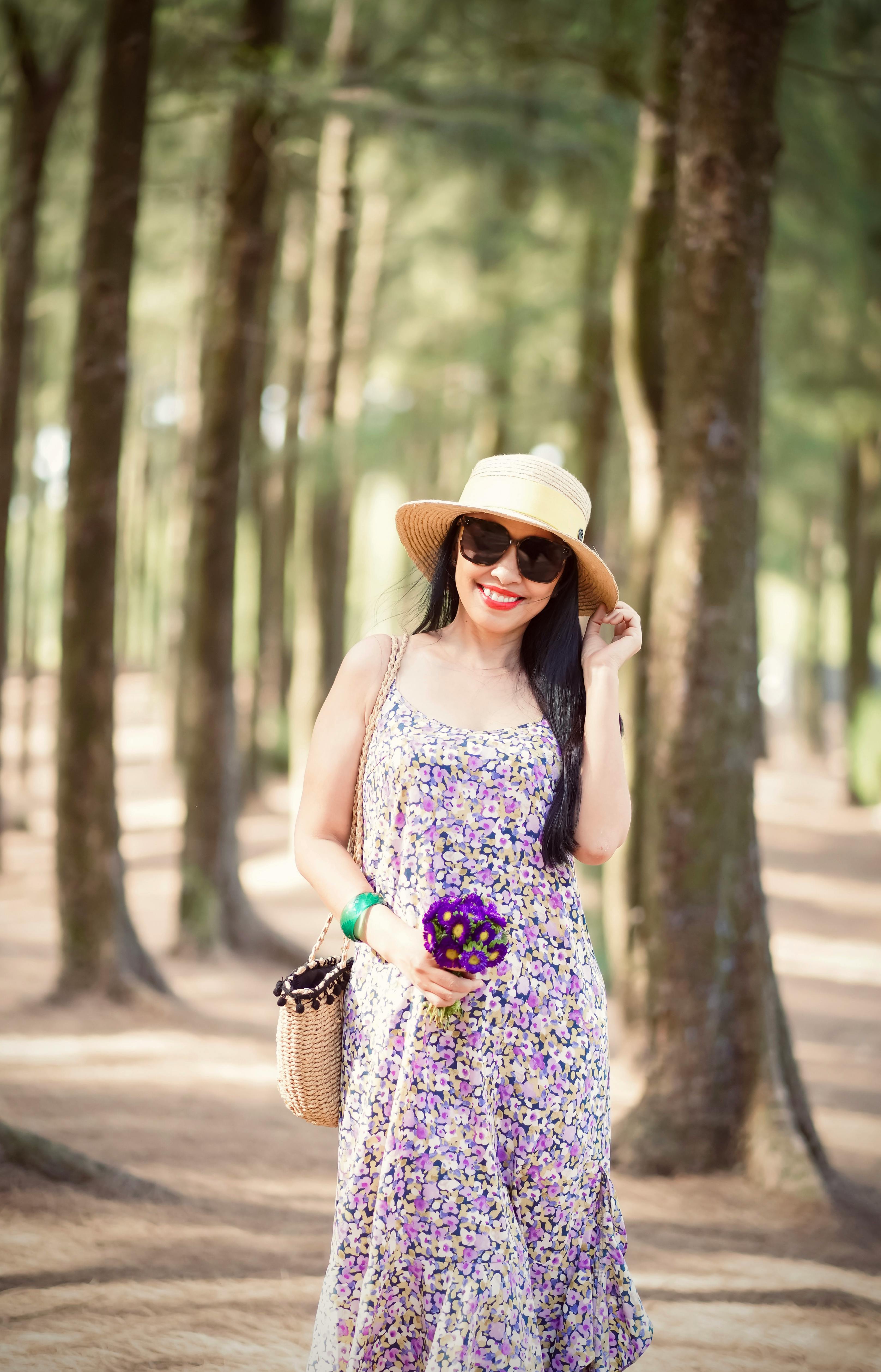 Free Woman wearing floral dress and sun hat smiling in a forest setting. Stock Photo