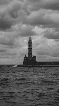 Black and white photo of a lighthouse with stormy clouds and rough sea.
