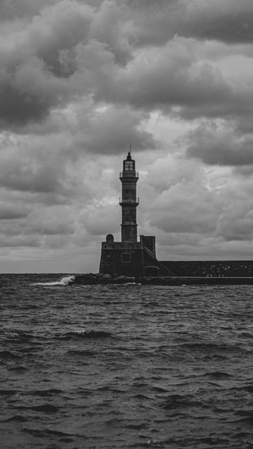Black and white photo of a lighthouse with stormy clouds and rough sea.
