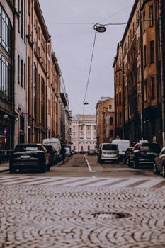 Cobblestone street with parked cars flanked by historic buildings, capturing an urban scene.