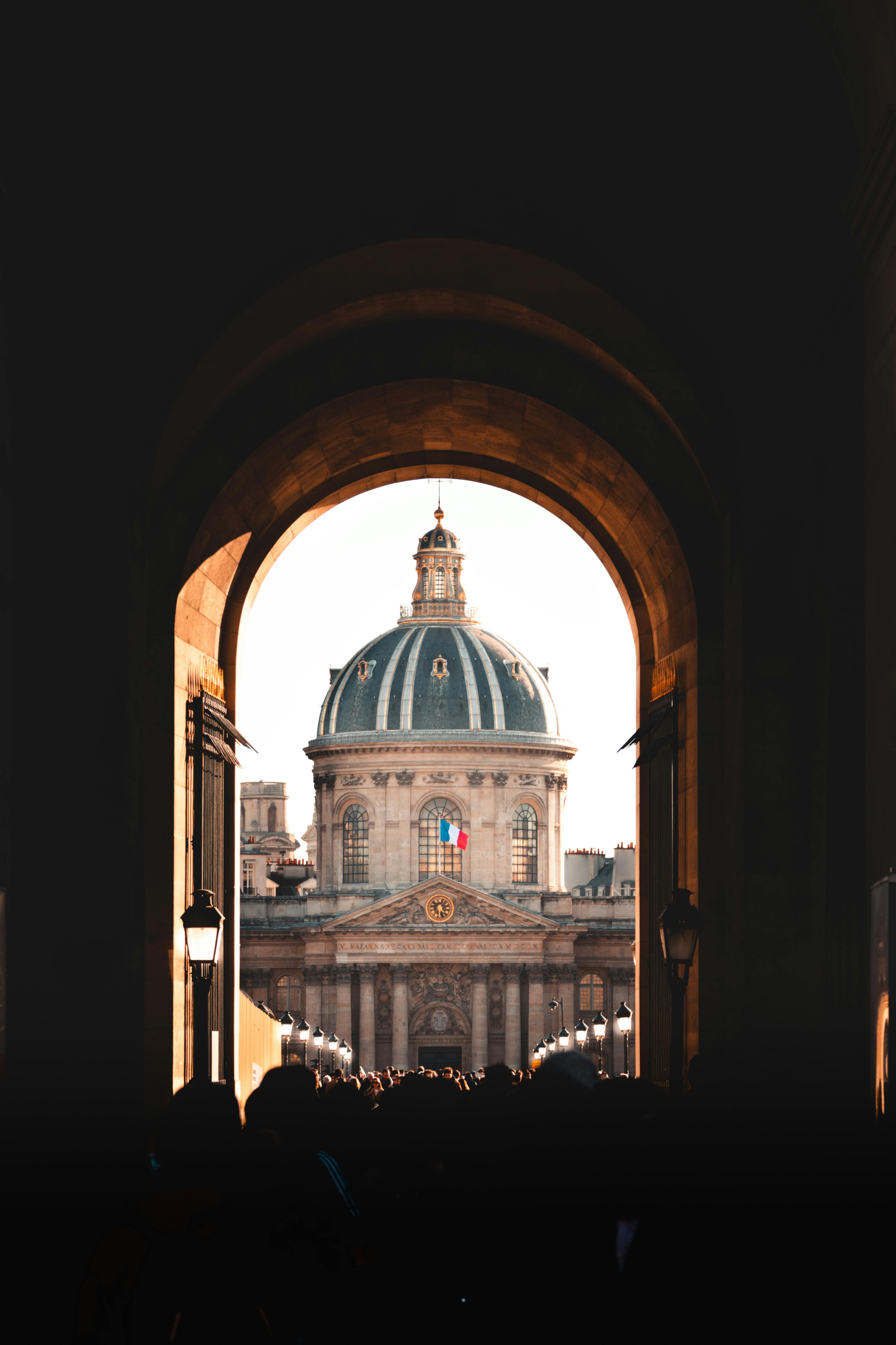 Dramatic view of the Institut de France framed by an archway in Paris, capturing a vibrant historical atmosphere.