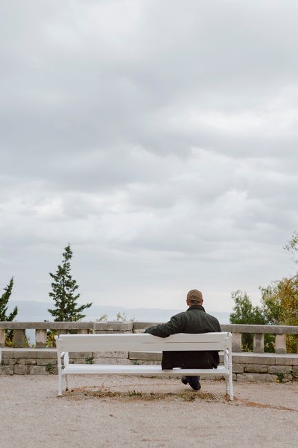 A solitary man sits on a bench against a cloudy sky, embracing peaceful solitude.