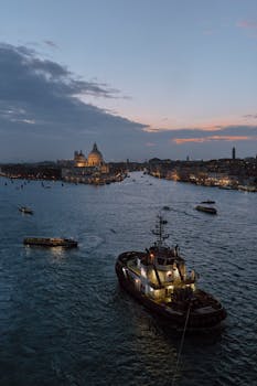 Twilight view of Venice with illuminated boats and iconic architecture under a dramatic sky.
