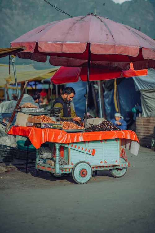 Free A street vendor selling various goods from a colorful cart in a lively outdoor market. Stock Photo