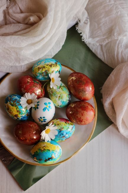 Colorful Easter eggs in a plate with daisy accents, perfect for spring decor inspiration.