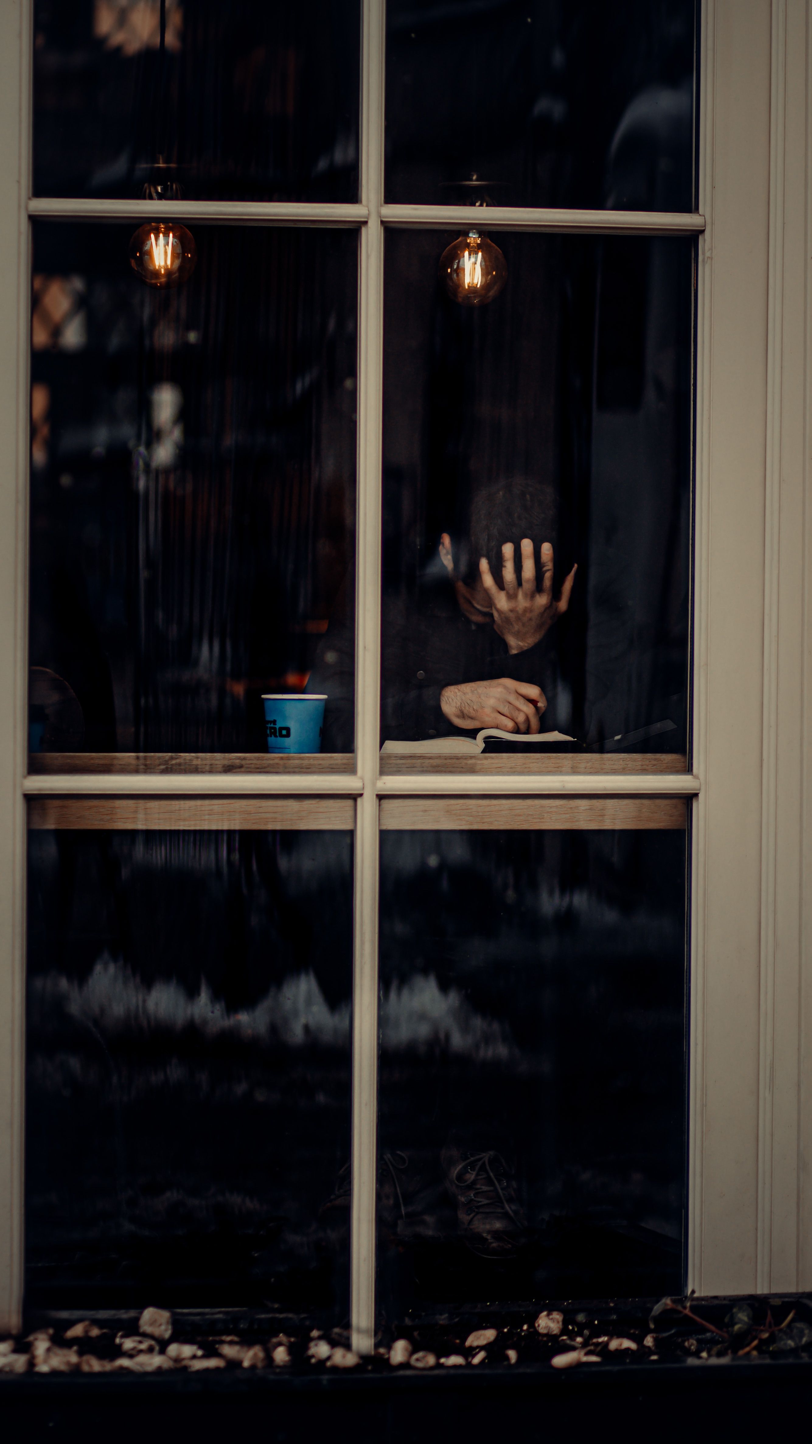 A man sits with hand on face at a window in Istanbul, exuding deep contemplation.