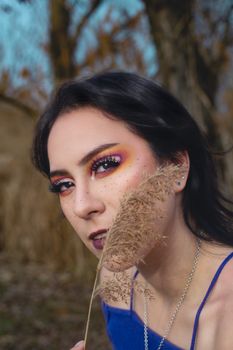 Close-up of a woman with striking eye makeup holding dry grass outdoors in Emilia-Romagna, Italy.