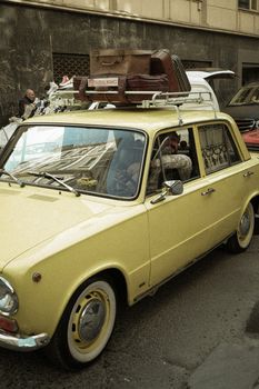 Classic yellow car with luggage on top, in a city street, capturing a retro travel vibe.