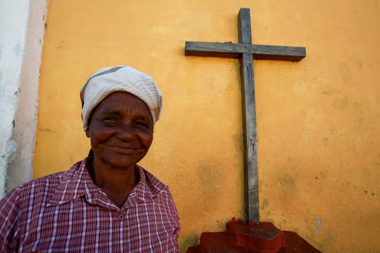 An Elderly Woman Standing Near A Wooden Crucifix