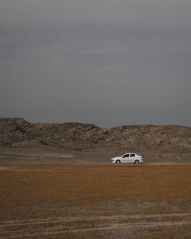 A white car travels through the arid desert landscape of Kish, Hormozgan Province, Iran, showcasing adventure and solitude.