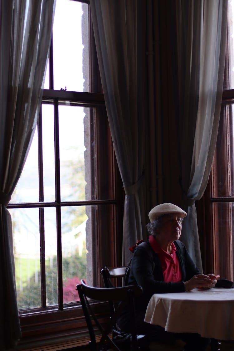 Person Wearing A Hat Sitting At A Table Near Windows