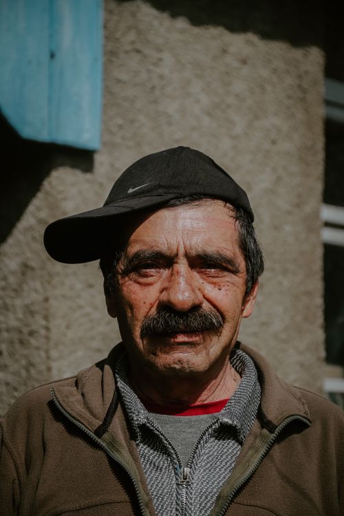 Free Close-up portrait of a senior man wearing a black cap and brown jacket outdoors. Stock Photo