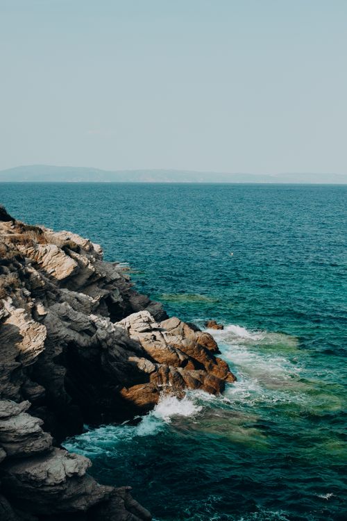 Free Discover the stunning rocky coastline of Greece, where eroded cliffs meet vibrant sea under a clear sky. Stock Photo