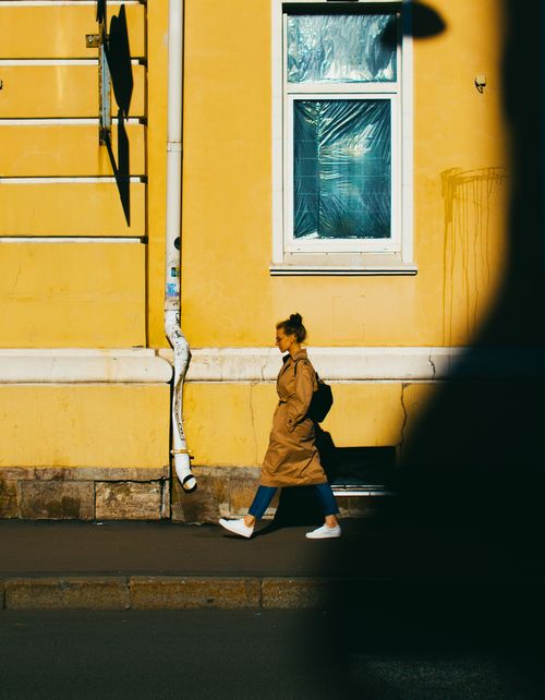 Free A woman walks along a yellow wall in Saint Petersburg, capturing urban life. Stock Photo