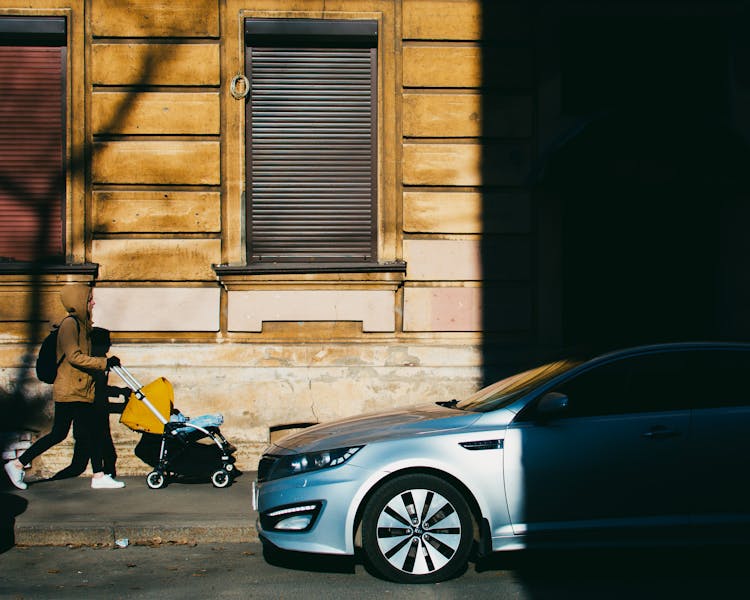 Woman In Brown Jacket Pushing A Stroller On The Sidewalk