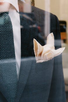 Close-up of a formal suit with a pocket square and necktie behind a glass pane.