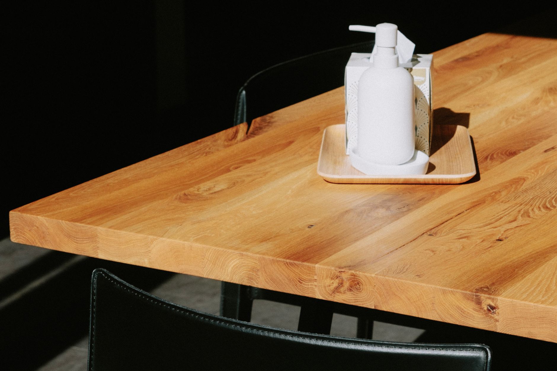 Simple wooden table with a white pump bottle and tissue box in natural light.