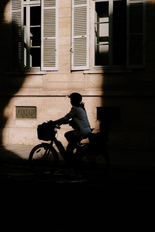 Woman Riding a Bicycle near a Building with Wooden Windows